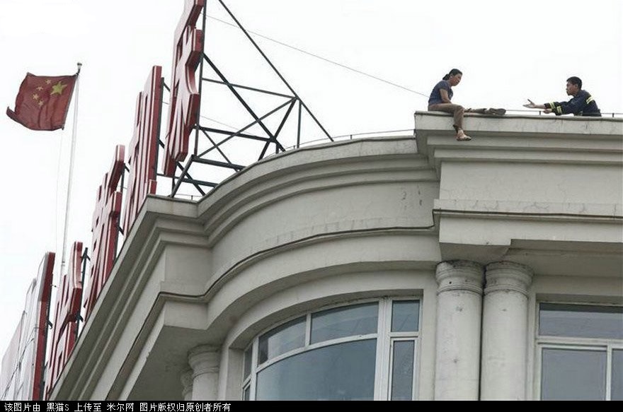 　2007年6月19日，遼寧瀋陽，營救人員正在勸說一名坐在屋頂上的婦女。這名婦女44歲，患有癌症，因無力承受醫療費用產生輕生念頭。